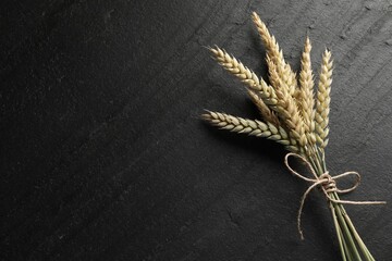 Bunch of wheat spikes on black table, top view. Space for text