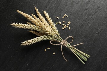 Bunch of wheat spikes and grains on black table, flat lay