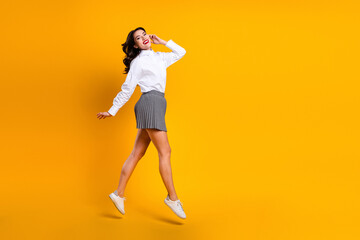 Confident young woman posing dynamically in a fashionable shirt and skirt against a vibrant yellow...
