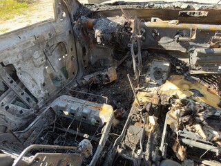 This image depicts the severely burned interior of a vehicle, showing extensive damage and charring to the seats, dashboard, and other components, consistent with a post-fire scene.