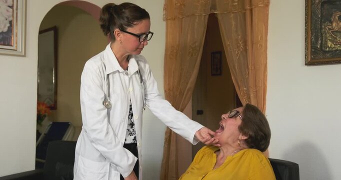 Healthcare worker examining elderly patient's throat during home visit, checking tonsils and oral cavity for signs of potential medical condition