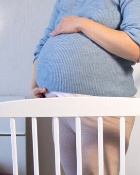 Pregnant Woman Preparing Baby Crib at Home Nursery Interior