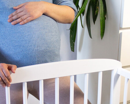 Pregnant Woman Preparing Baby Crib at Home Nursery Interior