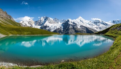 turquoise glacial lake reflecting snow capped mountains and meadows in alpine scenery