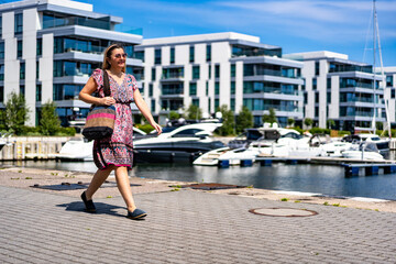 Portrait of middle-aged beautiful women walking around modern yacht port in seaside city on summer...