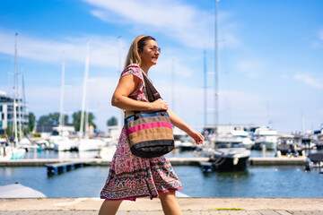 Portrait of middle-aged beautiful women walking around modern yacht port in seaside city on summer...