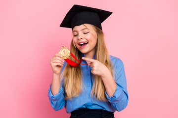 Young blonde girl in graduation cap holding gold medal against pink background celebrating her...