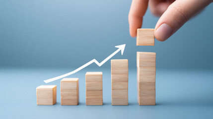 A hand places wooden blocks in ascending order, symbolizing growth and progress. An upward arrow emphasizes the increasing trend.	