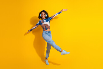 Joyful young woman posing energetically against a vibrant yellow background, expressing happiness...