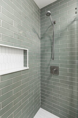 A bathroom shower with sage green subway tiles, chrome shower head, and a white picket tile shelf and flooring.