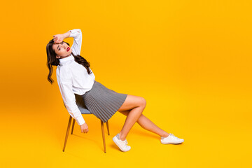 Exhausted woman in chic outfit sitting confidently on a chair against a vibrant yellow background...