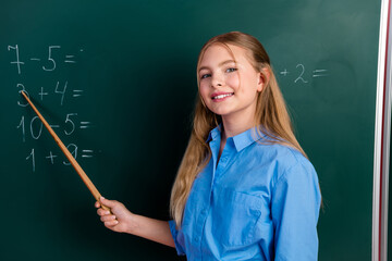 Cheerful young student pointing to math problems on the chalkboard during a classroom lesson in a...
