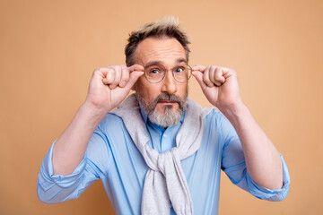 Confident mature businessman adjusting glasses against beige background showcasing elegant style...