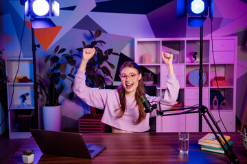 Popular female influencer enjoying live podcasting with colorful neon lighting in a modern home...