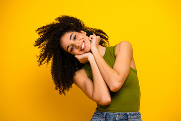 Young stylish woman with curly hair posing against a yellow background wearing casual green top and...