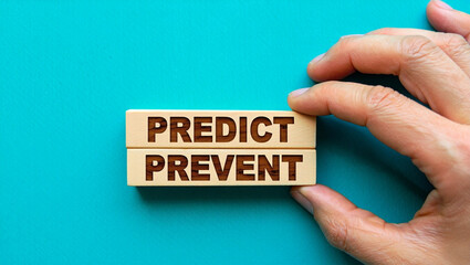 Human hand holding wooden blocks with the words predict and prevent stacked on a teal background symbolizing foresight and proactive measures