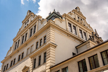 Historic Bavarian Architecture In Munich: Yellow Corner Building With Green Dome Tower, Ornate Windows, Flower Boxes, And Steep Roof Under Dramatic Cloudy Sky In European Urban Landscape