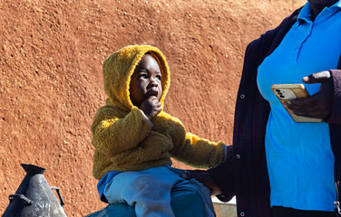 single african child in the africa village, mother on the phone, outdoors in front of the house,...
