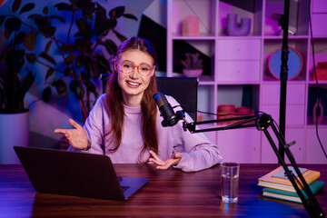 Cute female blogger hosting a live podcast with a microphone in a modern home office, illuminated...