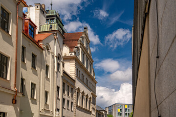Historic Bavarian Architecture In Munich: Yellow Corner Building With Green Dome Tower, Ornate Windows, Flower Boxes, And Steep Roof Under Dramatic Cloudy Sky In European Urban Landscape