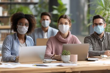 Contemporary lifestyle and workforce idea a diverse group of colleagues in masks collaborating on a project at a table in an office