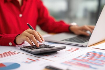 Businesswoman in red shirt using laptop and financial calculator analyzing statistics and charts in a modern office