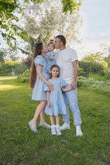 Fototapeta premium A happy family in nature. The family has two daughters. The family is dressed in blue clothes, and everyone is looking at the camera. 
