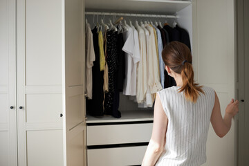 Woman choosing clothes from wardrobe in bright modern bedroom. 
Woman looking into closet full of...