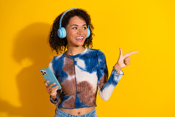 Young woman with headphones enjoying music, holding a phone and smiling, set against a vibrant...
