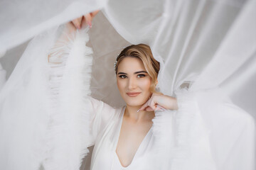 Bride in elegant white dress poses with soft fabric backdrop in a serene indoor setting