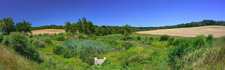 Panoramic photograph of a northern French hilly agricultural and natural landscape with a clear blue sky.