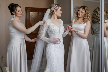 Bridesmaids assist bride with gown and veil during wedding preparations in cozy room