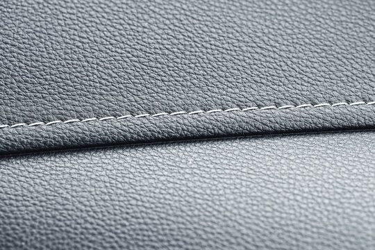 Close up of stitched leather texture. Gray surface with seam detail. Modern material background. Premium upholstery for car or furniture. High quality craftsmanship and industrial design.