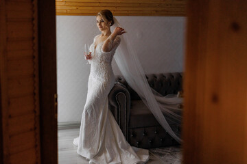 Bride preparing for her wedding day in elegant gown with a veil and glass of champagne