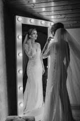 Bride preparing for wedding day in elegant dress before a mirror with lights