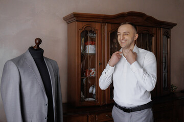 Man adjusting collar in front of a tailored suit on a mannequin in a stylish home setting