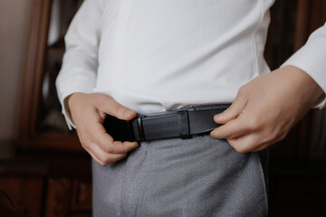 Man adjusting his belt while preparing for a formal event at home in the morning light