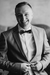 Man in a suit smiling while adjusting his bow tie indoors