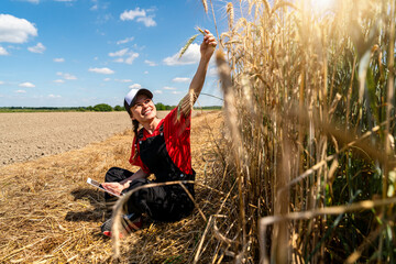 Female farmer with tablet sitting on ground by cereal field
