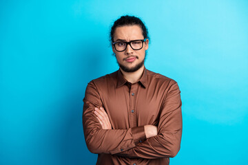 Confident man in stylish brown shirt with arms crossed against a vibrant turquoise background