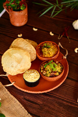 Luchi, Mix Vegetable and Dal Breakfast. A rustic platter of Indian snacks, including puri, pakora, and a small bowl of chutney, served on a wooden table.
