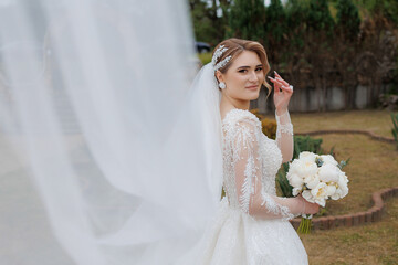 Bride poses elegantly outdoors while holding bouquet on her wedding day in a serene garden setting