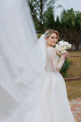 Bride in elegant wedding dress holding bouquet in garden setting during daytime event