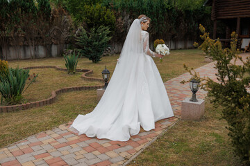 Bride in elegant white dress walks through garden path holding bouquet
