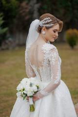 Elegant bride poses outdoors wearing a detailed wedding dress with a bouquet in hand