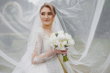 Bride holds bouquet while wearing elegant wedding dress in a soft misty environment