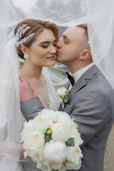 Couple shares a romantic moment under a veil on their wedding day in a serene outdoor setting