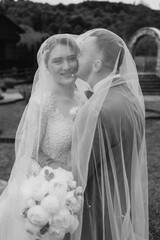 Couple embraces under veil during outdoor wedding ceremony at scenic location
