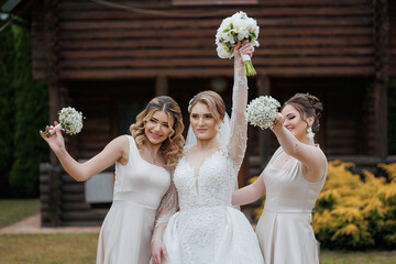 Three bridesmaids celebrate with a bride in front of a wooden house during a wedding
