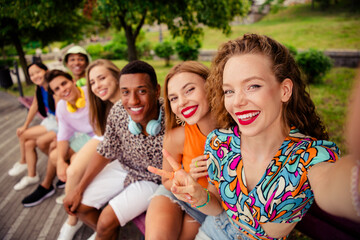 Group of cheerful young adults enjoying a sunny day outdoors, capturing memories together while...
